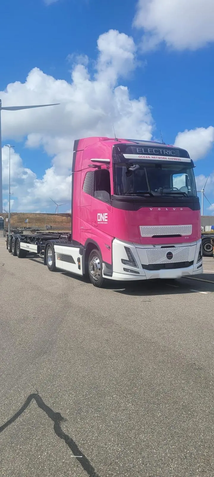 Electric Volvo FH with container chassis between wind turbines at the port